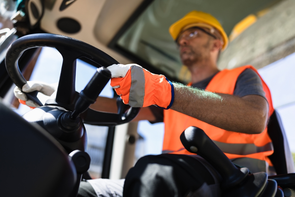 A construction or transport worker in a high-visibility vest and gloves operating heavy machinery.