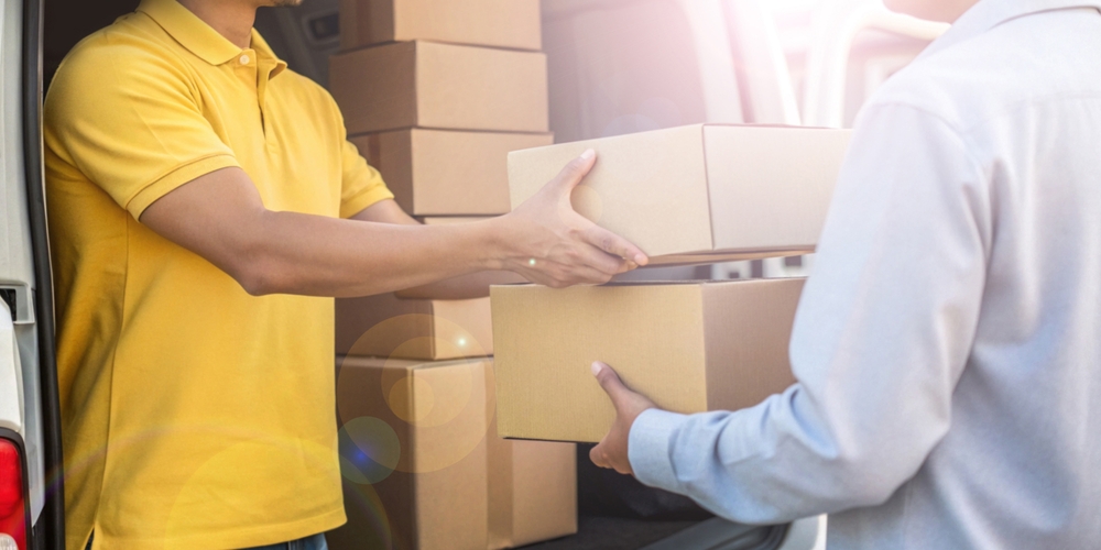 A delivery worker in a yellow shirt handing over a package to a customer from a van.